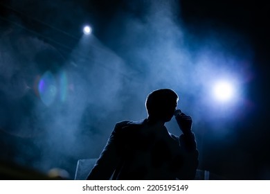 Singer silhoutte. Young vocalist singing in smoke on bright lit concert stage
