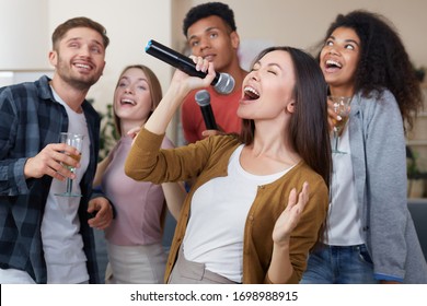 Singing Girl. Young beautiful asian woman holding microphone and singing while having fun with friends at home. Playing karaoke at home. Happy multicultural people spending time together - Powered by Shutterstock