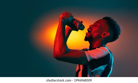 Singing, performing. African-american young man's portrait on red studio background in neon light. Beautiful male model rapping. Concept of human emotions, facial expression, youth, sales, ad. - Powered by Shutterstock