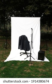 singing stage setup in a park with mic ,speaker and jacket hanging on a chair with white back drop 
