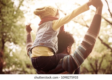 Single African American Father Carrying His Daughter On Shoulders In Park.