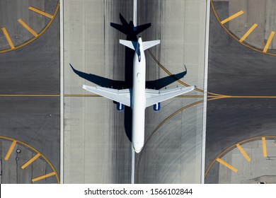 Single aisle aircraft landing at international airport runway in the center of the frame. Aerial view with symmetrical yellow lines. Travellers starting or finishing their trips.