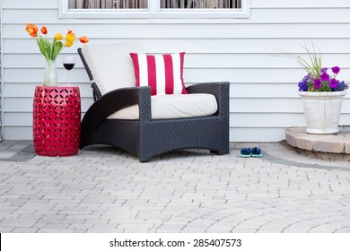 Single Armchair With A Red Ceramic Pedestal Table And Vase Of Spring Tulips With A Matching Striped Red And White Cushion On A Brick Paved Outdoor Patio For A Relaxing Break