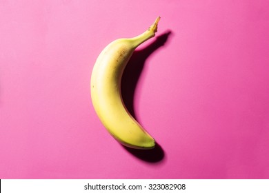 Single banana on a pink background with strong shadow - Powered by Shutterstock