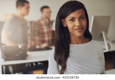 Single Beautiful Female Business Owner Wearing Black And White Striped Blouse With Two Employees On Computer In Background