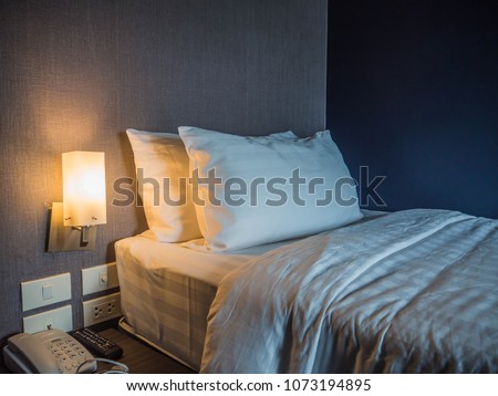 Single bed  and two pillows white cotton blanket with warm light in a cosy bed room .