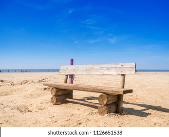 Single bench made of solid wooden planks on the East Frisian North Sea beach in summery blue sky.