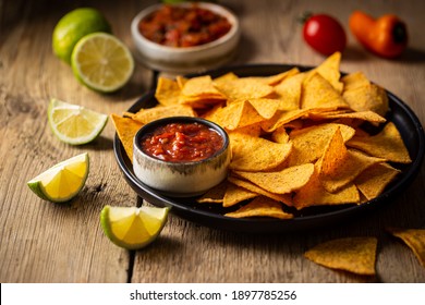 Single big black plate of yellow corn tortilla nachos chips with salsa sauce over wooden table - Powered by Shutterstock