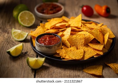 Single big black plate of yellow corn tortilla nachos chips with salsa sauce over wooden table