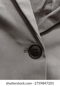 Single black button on a grey wool blazer with visible lapel fold and lining