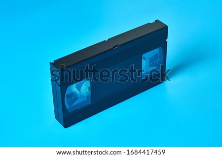 Single black old plastic vhs video cassette lies on blue desk. Concept of 90s. Close-up