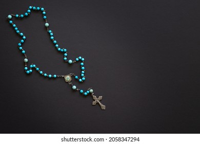 Single blue rosary on a black background with copy space