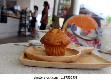 A Single Blueberry Muffin Shot In The Context Of A Cafe Interior With Customers Queuing In The Background.