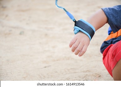 Single Boy's Hand Holding With Blue Leash During Activity Or Playing Outside In Public Place, With Background Sand. Kid Leash Safety Concept.