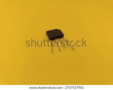Single bridge rectifier diode with four metal terminals on yellow surface. High-quality electronic spare part for AC to DC power conversion and circuit board assembly.