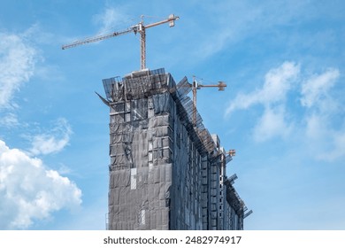 Single building under construction with gray protection nets, cranes, blue sky - Powered by Shutterstock