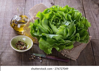 Single butter lettuce head, oil and seasoning over rustic wooden background