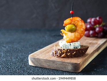 Single classic Spanish tapas lie on a wooden board. The tapas consist of shrimp, gorgonzola, green olive and bruschetta skewered for canapes - close-up
