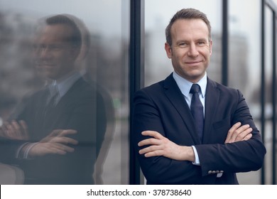 Single confident and handsome male businessman in blue suit and necktie with grin leaning on window outdoors