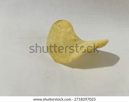 A single, crispy potato chip with a distinct curve, casting a shadow on a clean, plain white background. It highlights the snack's texture.