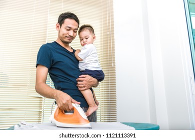 Single Dad Is Ironing While Carrying His Son. People And Lifestyles Concept.