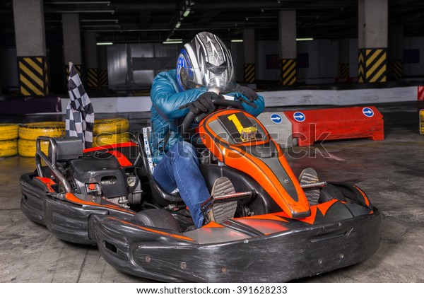 Single\
defeated bumping car racer in blue coat, jeans and safety helmet\
with head down on arms over steering\
wheel