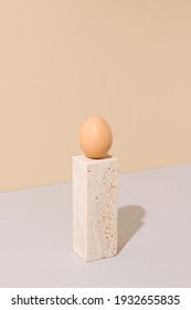 Single egg standing on a travertine marble block on a beige and gray background. 2021 Easter unique still life composition. Surreal retro creative organic food concept.
