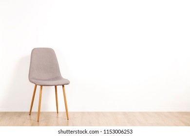 Single Elegant Gray Loft Style Chair Standing Alone On Wooden Floor In Empty Room, Big Blank Wall Background. Large Copy Space For Text. Only One Vacant Seat. Human Resources Hiring Campaign Concept.