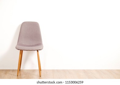 Single Elegant Gray Loft Style Chair Standing Alone On Wooden Floor In Empty Room, Big Blank Wall Background. Large Copy Space For Text. Only One Vacant Seat. Human Resources Hiring Campaign Concept.