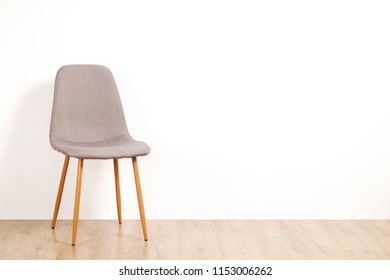 Single Elegant Gray Loft Style Chair Standing Alone On Wooden Floor In Empty Room, Big Blank Wall Background. Large Copy Space For Text. Only One Vacant Seat. Human Resources Hiring Campaign Concept.