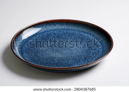 A single, elegant oval ceramic plate with a deep blue speckled glaze and a rich brown rim, presented on a neutral background.