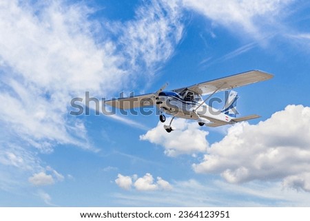 Single engine ultralight plane flying in the blue sky with white clouds