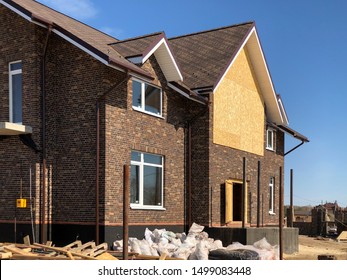 A Single Family Home Under Construction. The House Has Been Framed And Covered In Plywood. There Is A Two Car Garage With A Gravel Driveway.