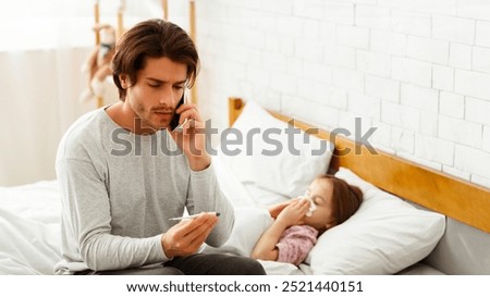 Single father checking his ill daughter's temperature with a thermometer in bed, girl having flue, father calling doctor, care concept, copy space