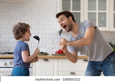 Single father dancing listen to music together with son hold kitchen spoon like microphone singing enjoy cooking in kitchen at home, turned routine into fun, food preparation everyday activity concept