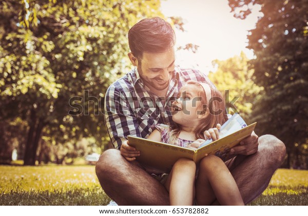 幼い娘と草の上に座り 本を読む父親 父の膝の上に座る少女 の写真素材 今すぐ編集