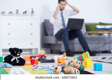 Single father sitting on a sofa in a nursery with toys on the floor