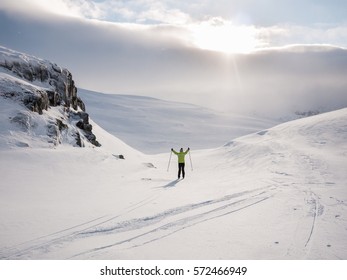 Single female cross-country skier off piste in the norwegian mountains with heavy clouds with the sun hiding at the edge passing some sun rays smoothly enlightening the flat terrain