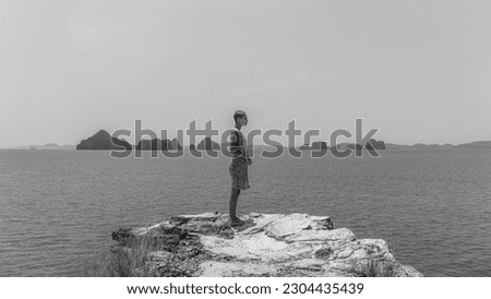 Single female model with bold stylish hairstyle in yellow summer dress standing at the edge of a cliff with wide open sea view in the background during a beautiful sunny day. 