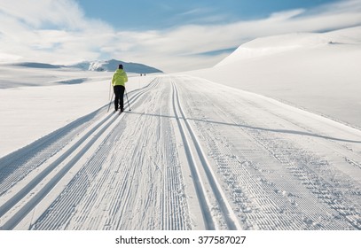 Single female skier following a double  groomed track up hill  during a cold day in the Norwegian Mountains at easter heading for summits in background