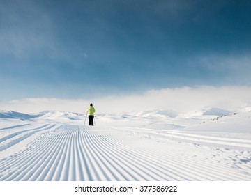 Single female skier following a well prepared groomed track during a cold day in the Norwegian Mountains at easter heading for summits in background