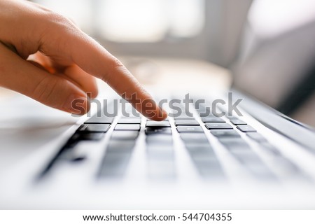 Single finger press button on laptop keyboard, close up clean image with sun flare