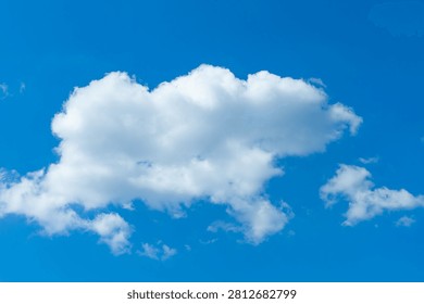 A single fluffy cloud moves slowly across the blue sky in the afternoon. The sun shines brightly and the weather is clear with a light breeze.