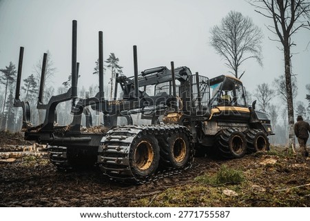 A single forestry forwarder machine is positioned in a cleared woodland area after logging activity. The vehicle is empty and not carrying any logs, offering a clear view of its structure and loading frame. The surrounding landscape shows freshly cut trees, branches, and uneven ground, typical of active forestry operations. The overcast sky and light fog add a subdued atmosphere to the scene. This image represents modern logging practices, forestry technology, and the balance between industrial activity and natural environments. With no workers present, the focus remains on the machine and its role in timber transport. Suitable for illustrating forestry industry, environmental topics, heavy equipment, and rural land use.