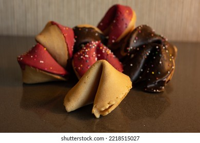 Single Fortune Cookie Sits In Front of Pile of Decorated Cookies on glass surface