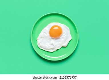 Single fried egg in a plate minimalist on a green table. Top view with a fried egg isolated on a colorful background.
