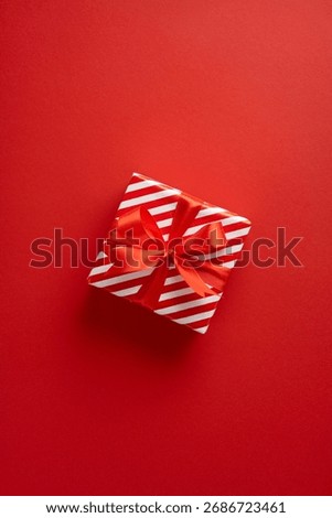 A single gift box with red and white stripes rests on a bold red backdrop. Vertical composition conveys festive mood, Christmas and New Year celebration, gift exchange, and holiday spirit