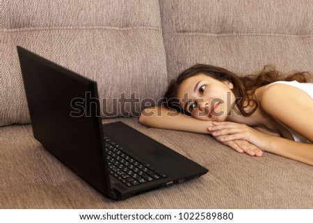 Single girl searching online content in a laptop lying on a couch in the living room at home.