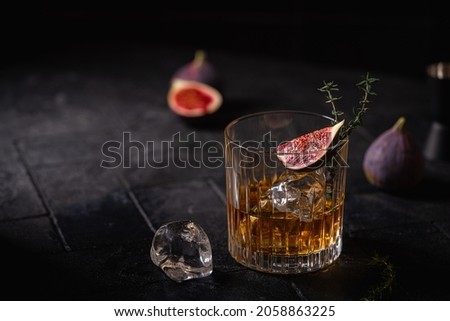 Single glass of whiskey with ice and figs on black background