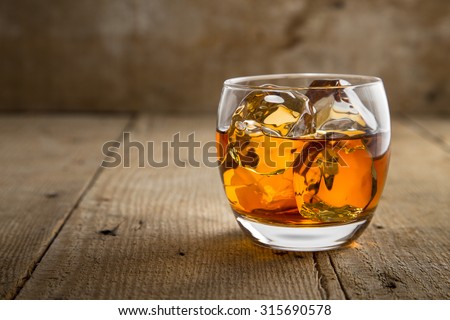 Single glass of whisky bourbon on the rocks golden on old rustic wooden surface open space